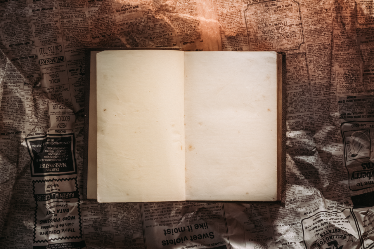 services-03 An open blank book placed on vintage crumpled newspapers, softly lit.