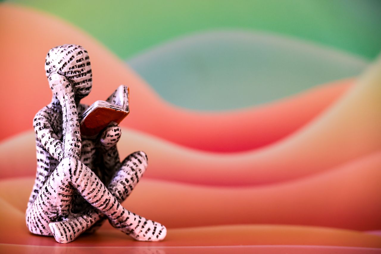Colorful art piece featuring a sculpture figure reading a book in front of vibrant abstract waves.
