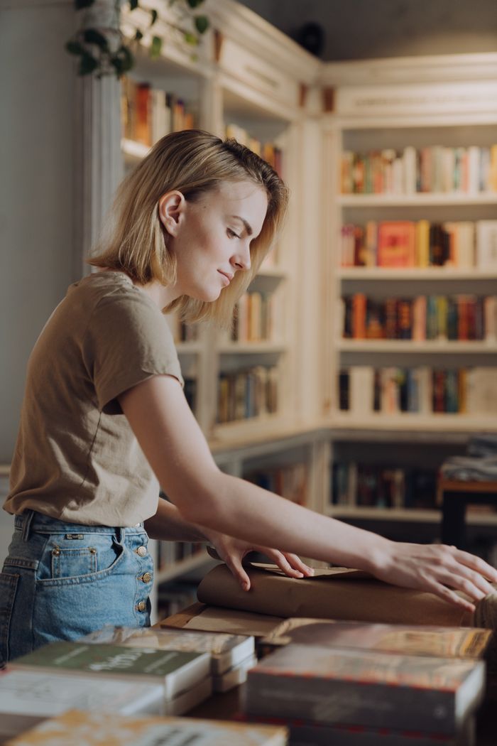 Young woman wrapping books in a cozy bookstore, showcasing a blend of work and literature.
