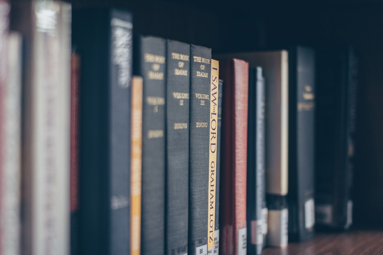 who-we-are A focused view of books on a library shelf featuring various titles in soft lighting.